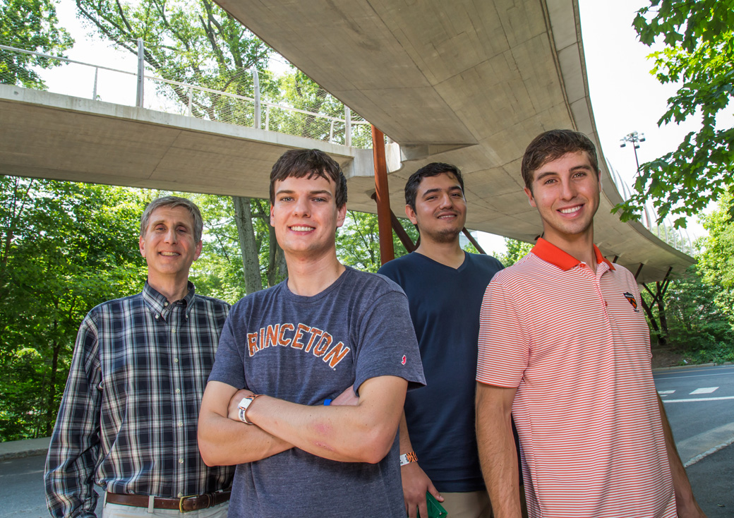 Professor James Sturm, Campbell Weaver, Levent Aygun and Matthew Gerber pose under a footbridge on Princeton's campus.