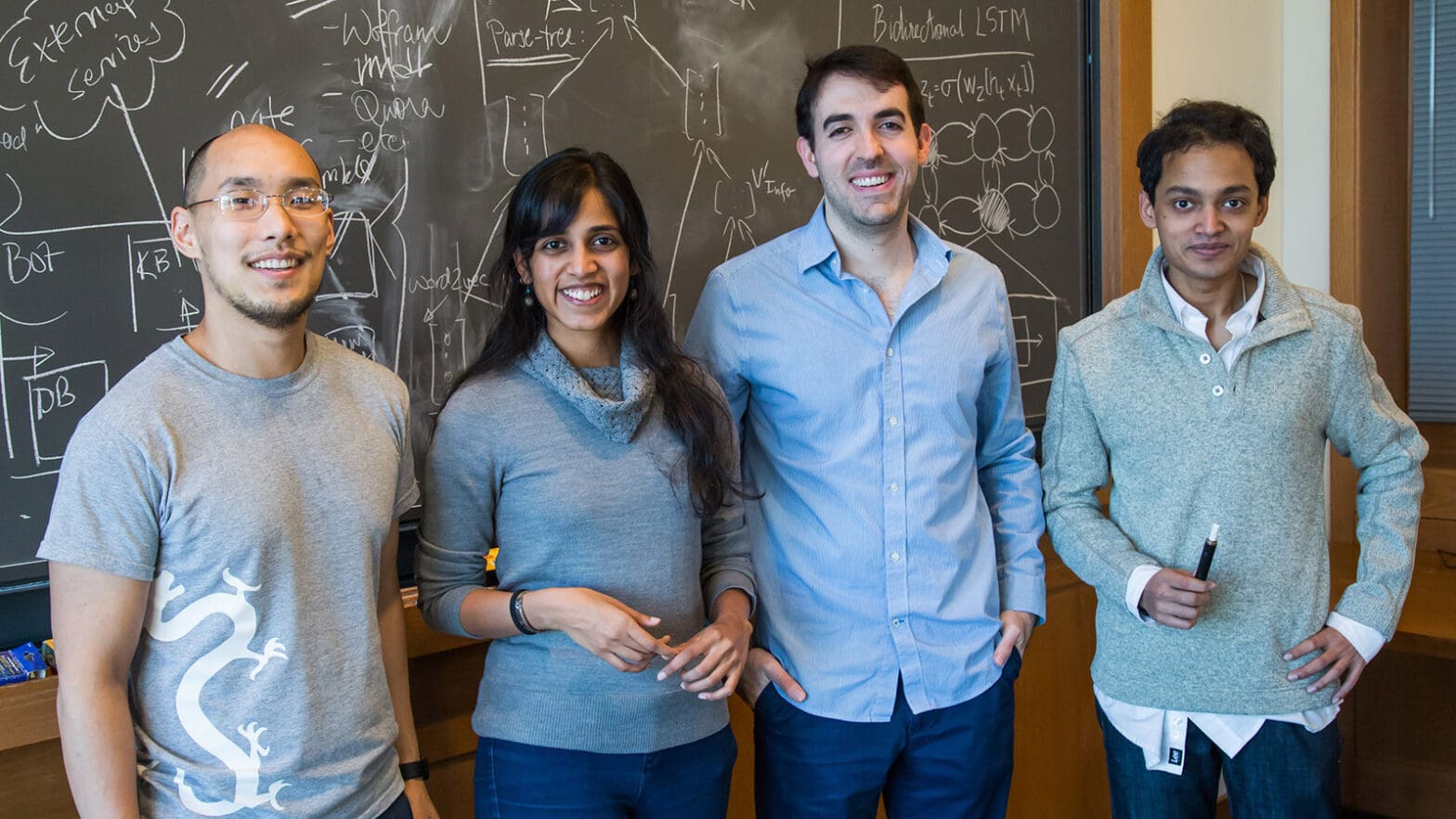 four students face camera in front of blackboard