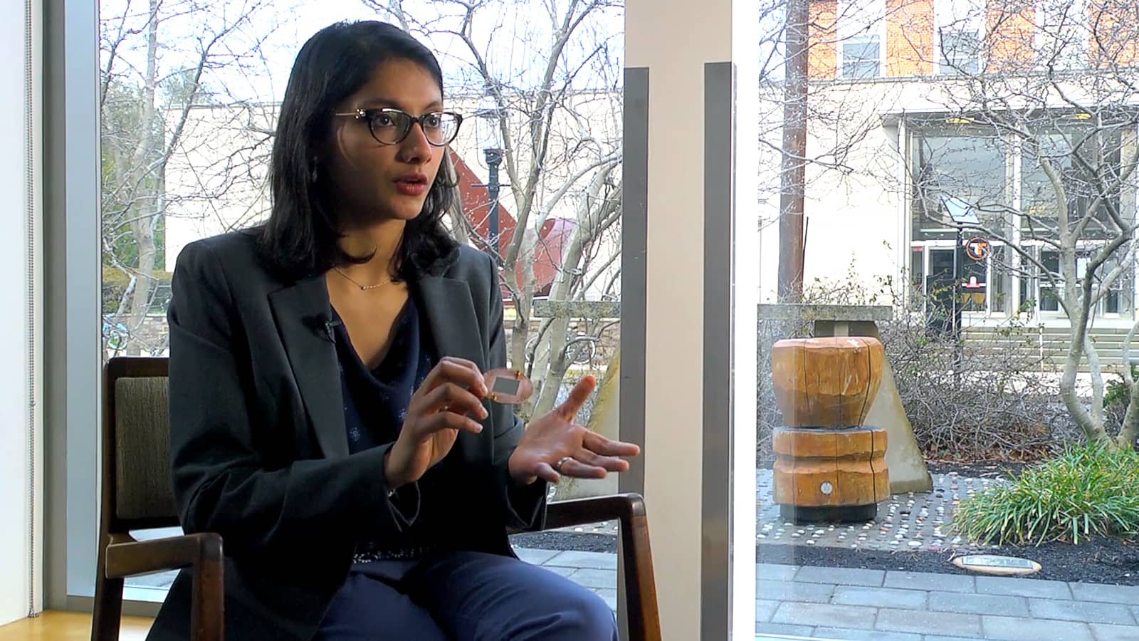 Neereja Sundaresan discusses her research, sitting in front of a window, with the main entrance of the Engineering school in the background.