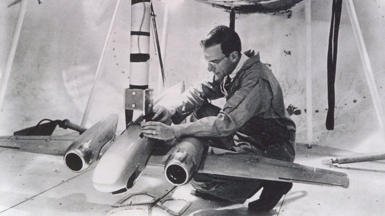 Research kneels while working on large model airplane (black and white)