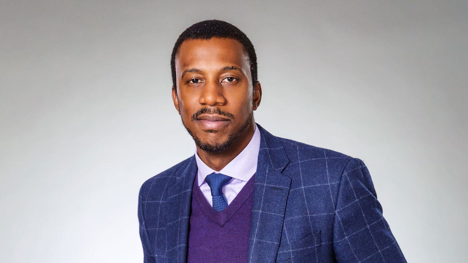 Rodney Priestley in a blue check sportcoat, blue tie, and purple v-neck sweater