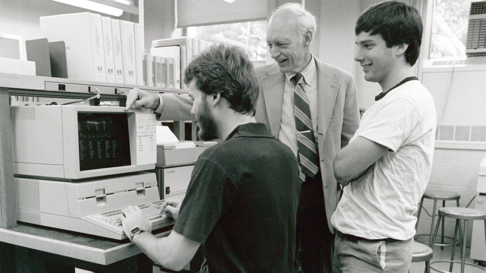 three men work at a 1980s personal computer
