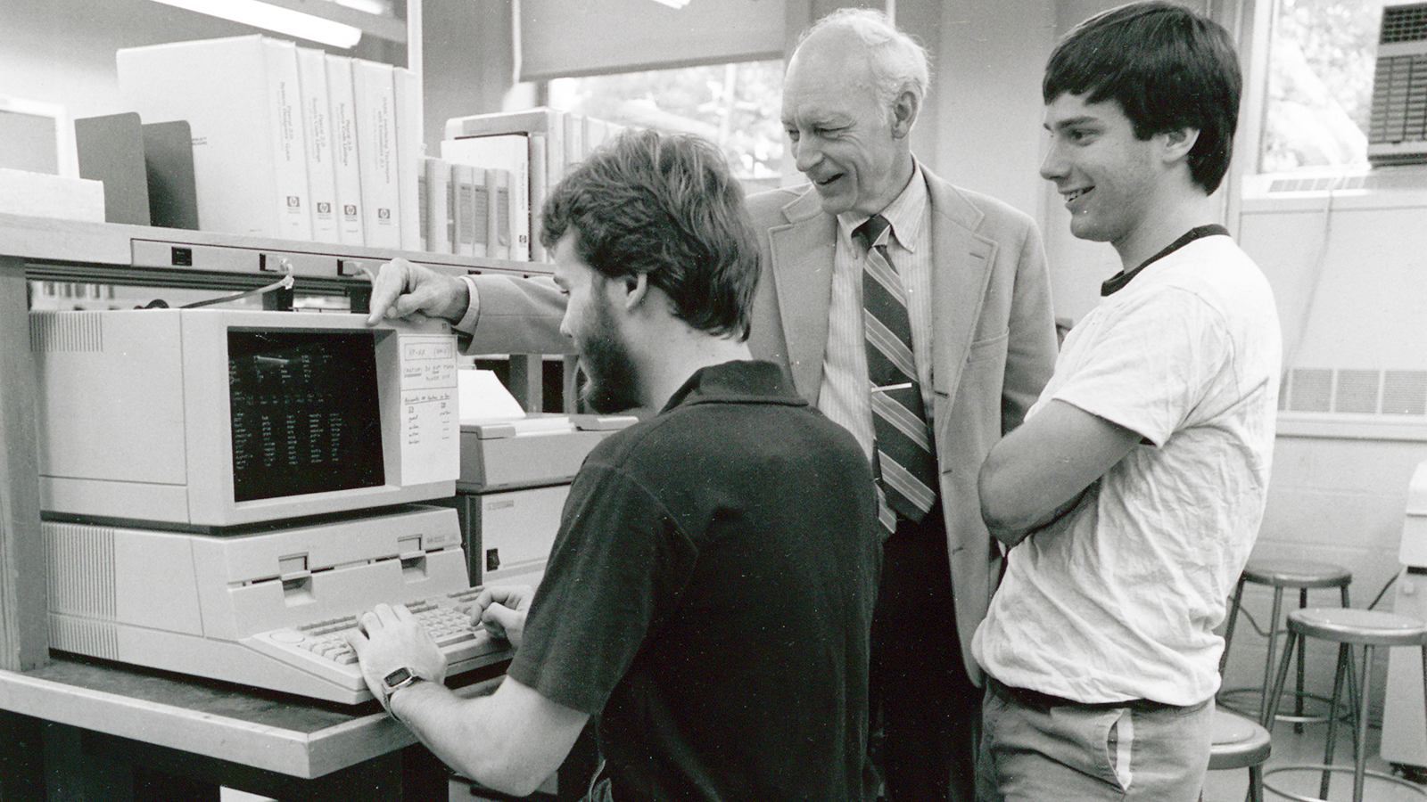 three men work at a 1980s personal computer