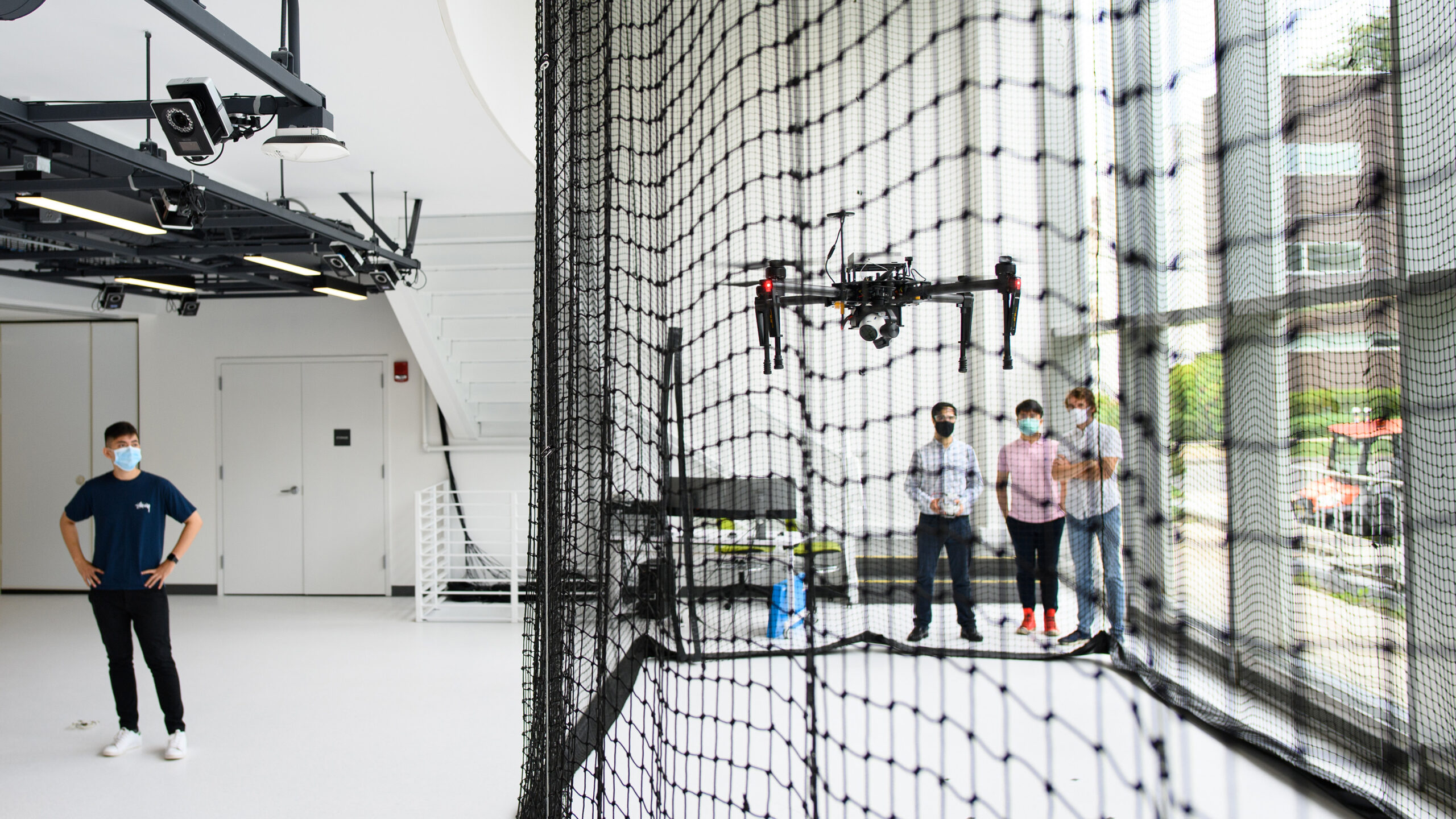People fly a drone indoors behind a mesh wall