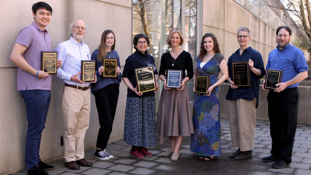 Eight people, each holding award plaques