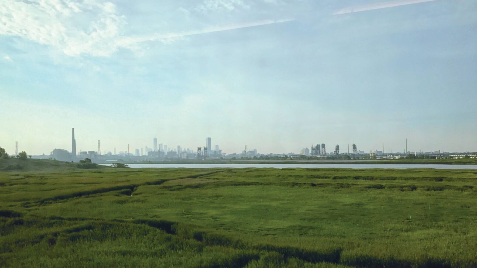 Photo of a city from afar, with grass in foreground. This is the Meadowlands.