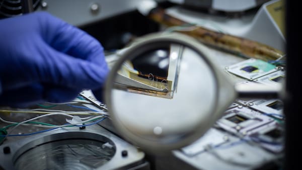 magnifying glass reveals the corner of a solar cell in tweezers