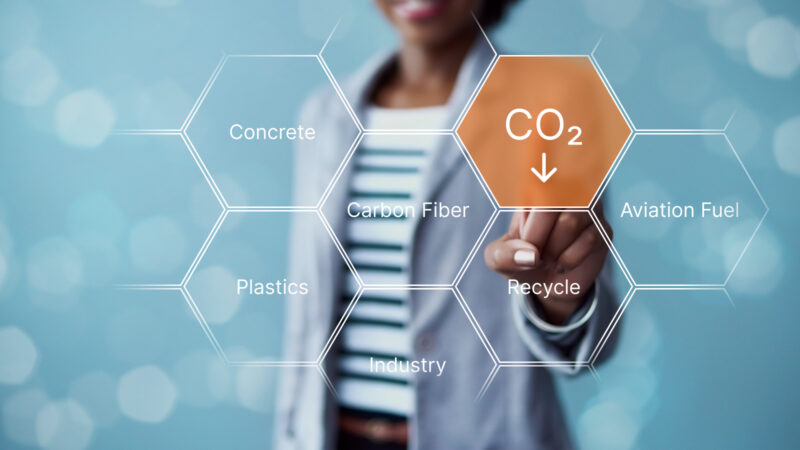 Illustration of person in background touching a network of hexagons, each containing words related to the reuse of carbon dioxide, such as concrete and aviation fuels