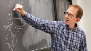 Professor draws physics diagram on chalkboard