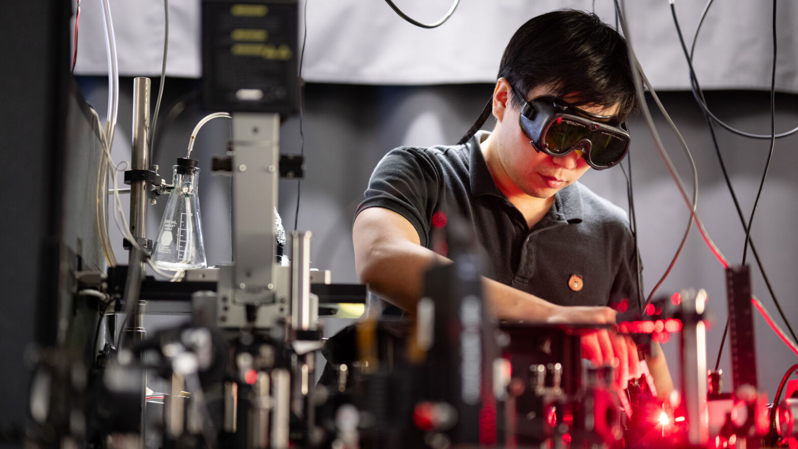 Researcher wearing goggles operates a laser surrounded by lab equipment