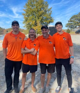 Four men posing in orange shirts