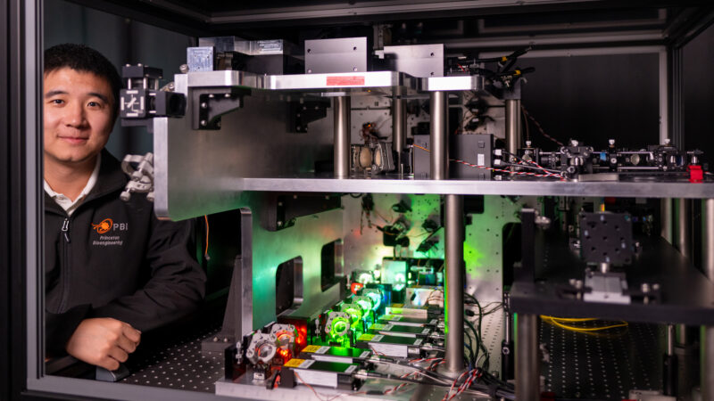 Researcher standing by equipment cabinet holding a setup of lasers and mirrors