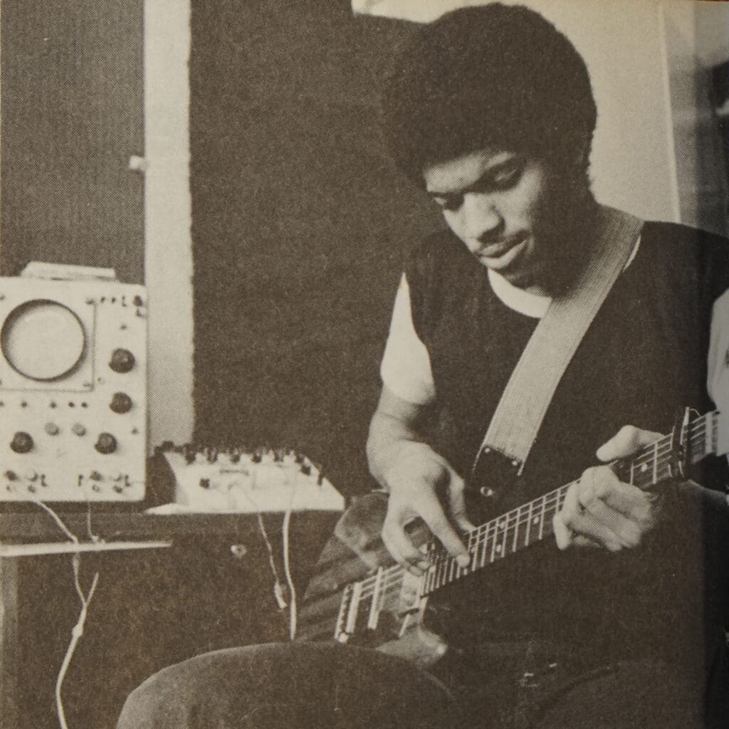 Black and white photo of Stanley Jordan as a college student. He is holding an electric guitar, with equipment behind him.