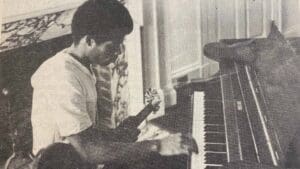 Stanley Jordan in his student days, playing piano, with an electric guitar across his lap. This is a black and white photo.