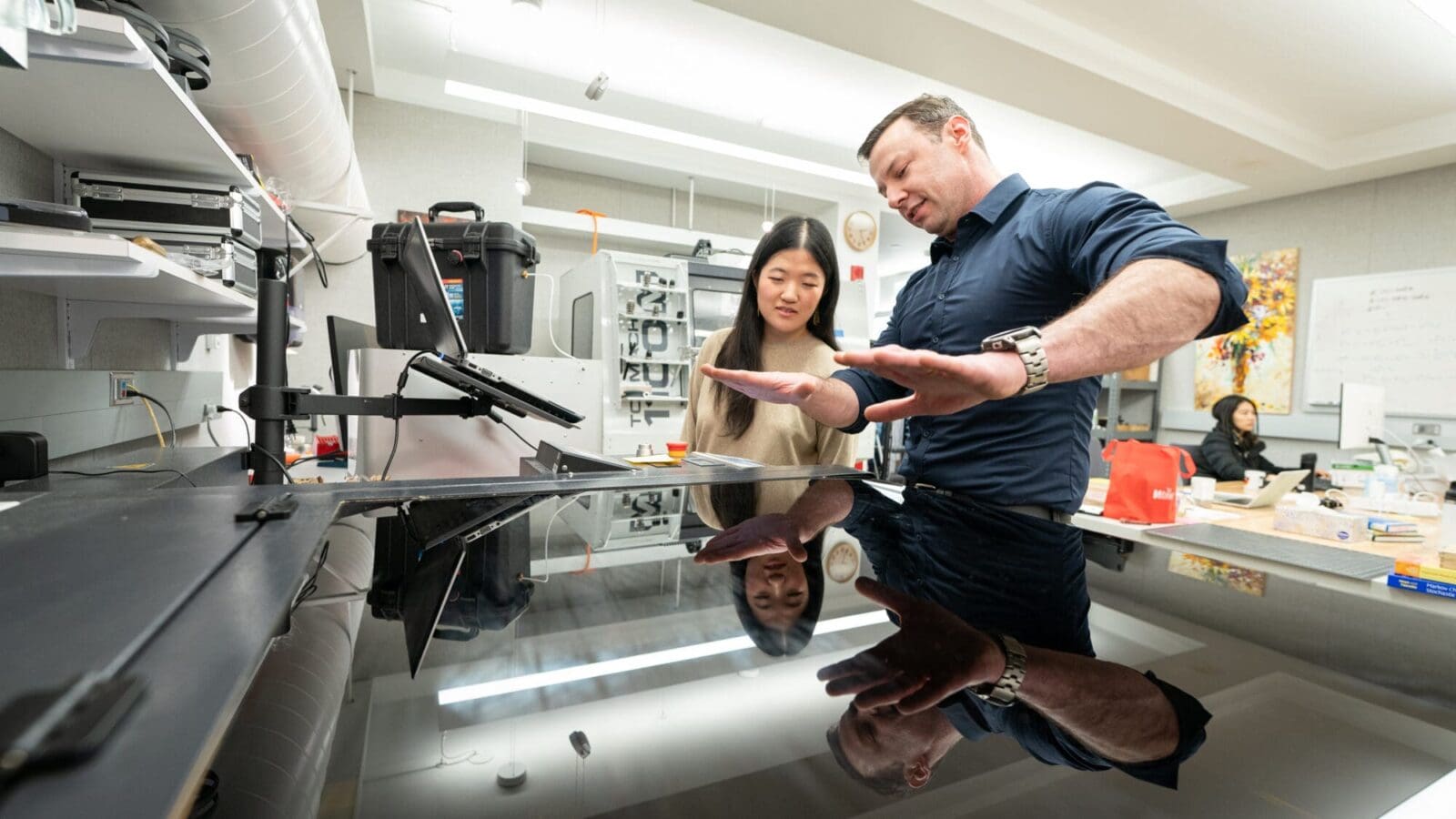 Male researcher flattens his hands above glass-topped machine while female researcher looks on