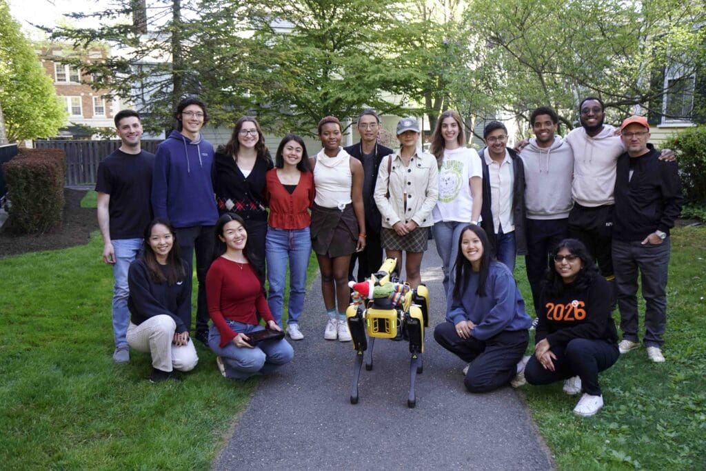 Outdoor class photo. The students and professors are gathered around the robot.