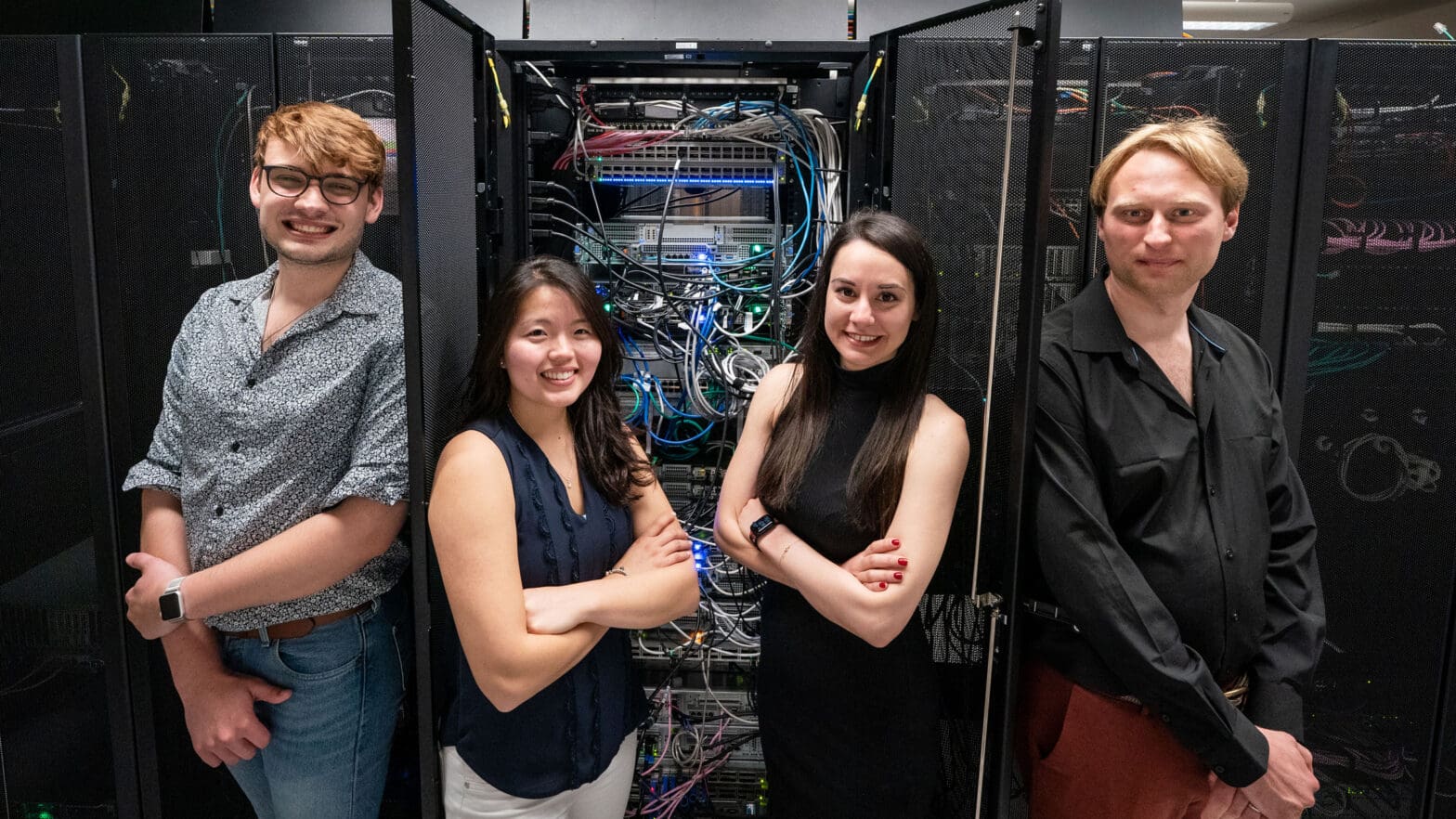 Four researchers standing in front of a computer server with wires showing.