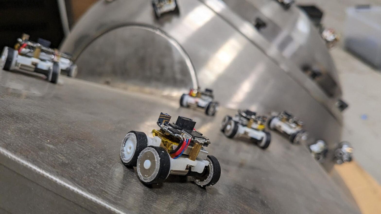 Small robotic vehicles move across metallic machinery.