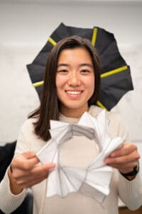 Sydney Hsu holding a prototype of an origami-based umbrella-like device for de-orbiting a small satellite.