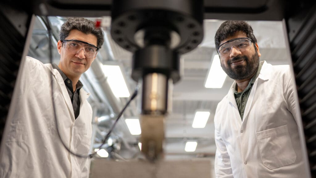 Two researchers face the camera with testing press in the foreground. 