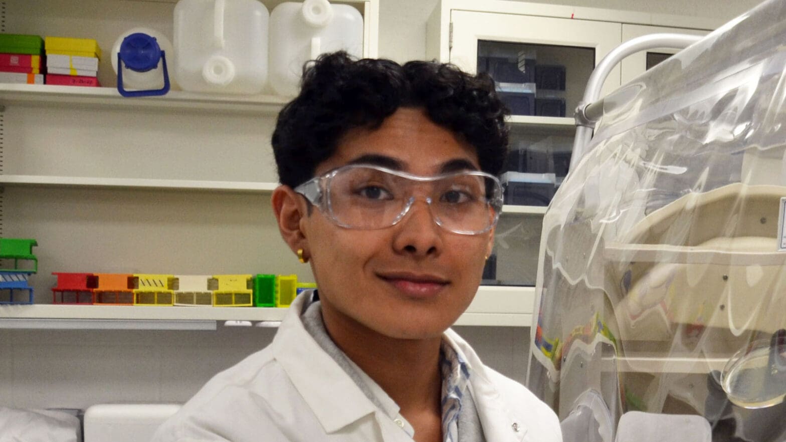 Anherutowa Calvo wearing safety glasses and a white coat in a laboratory.