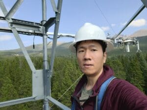 Man wearing hardhat stands on a metal tower in a forest