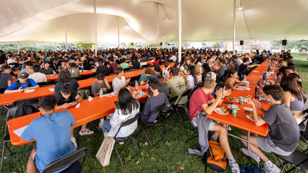 Many people at tables under large tent.