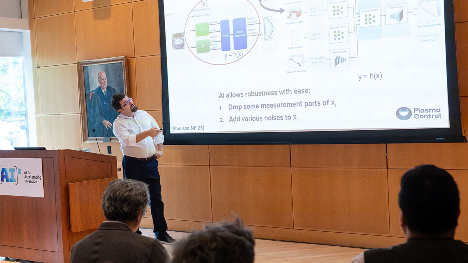 Man speaks near podium while pointing at a scientific graphics on a screen.