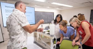 Man demonstrates experiments on table while group of women observe.