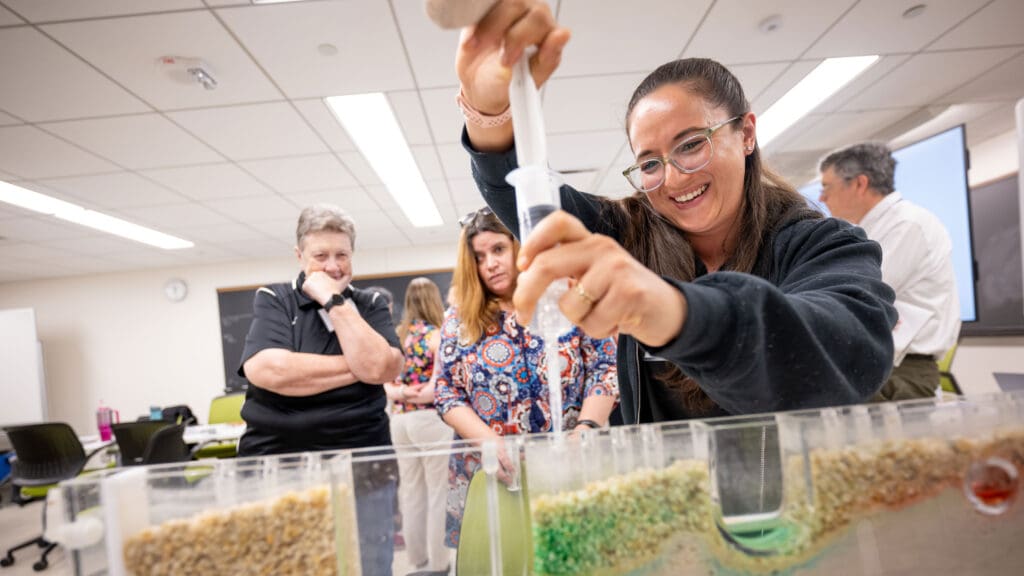 A woman injects dye from a syringe into a sandbox hydrology model