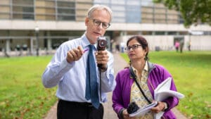 A man holding a handheld heat sensor stands next to a woman with a clipboard