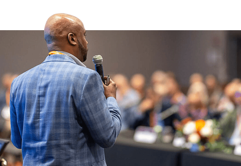 View from behind a man holding a microphone, presenting to an audience