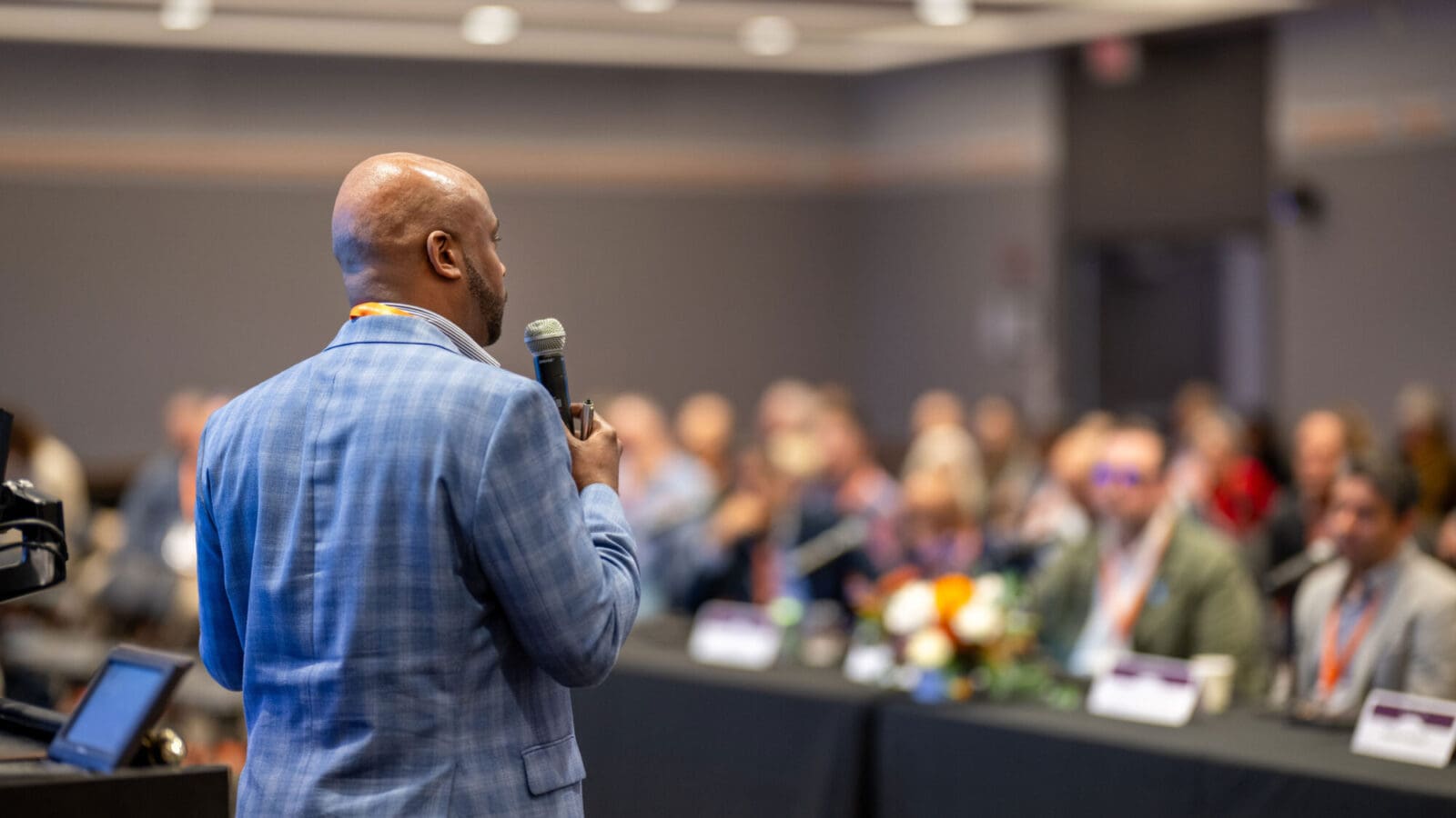 View from behind a man holding a microphone, presenting to an audience