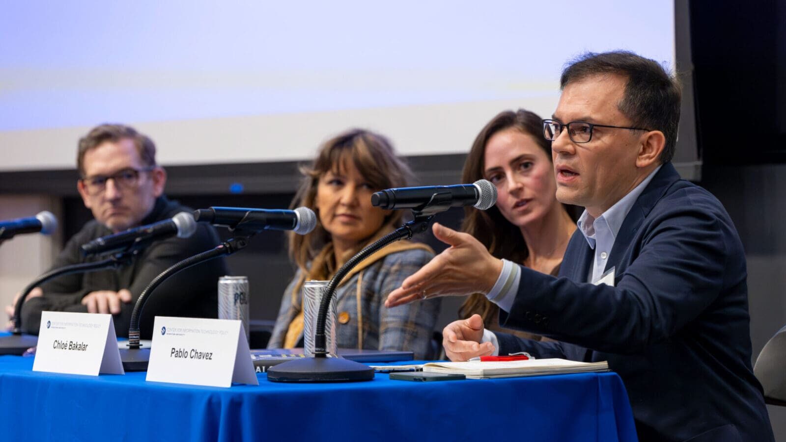 A group of panelists sit behind a table as one man addresses the audience