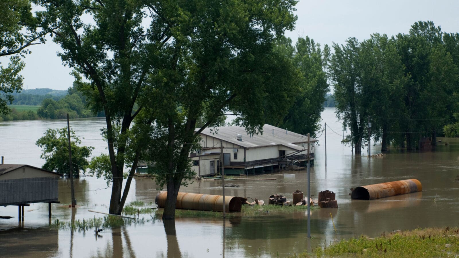 Flooded farmhouse with debris in the water in the foreground