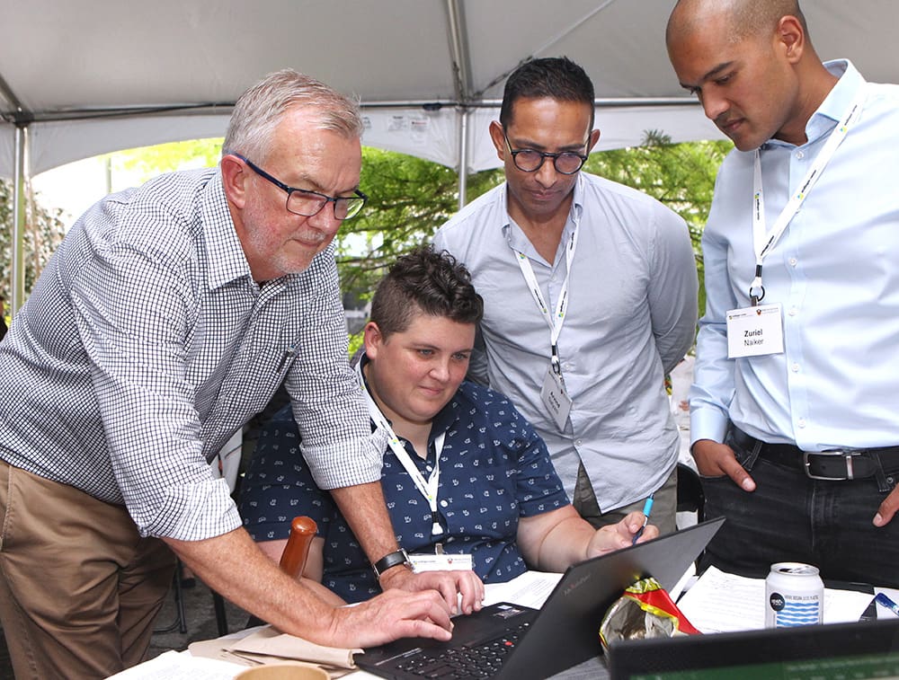 Standing man bends over laptop computer as three other people watch.