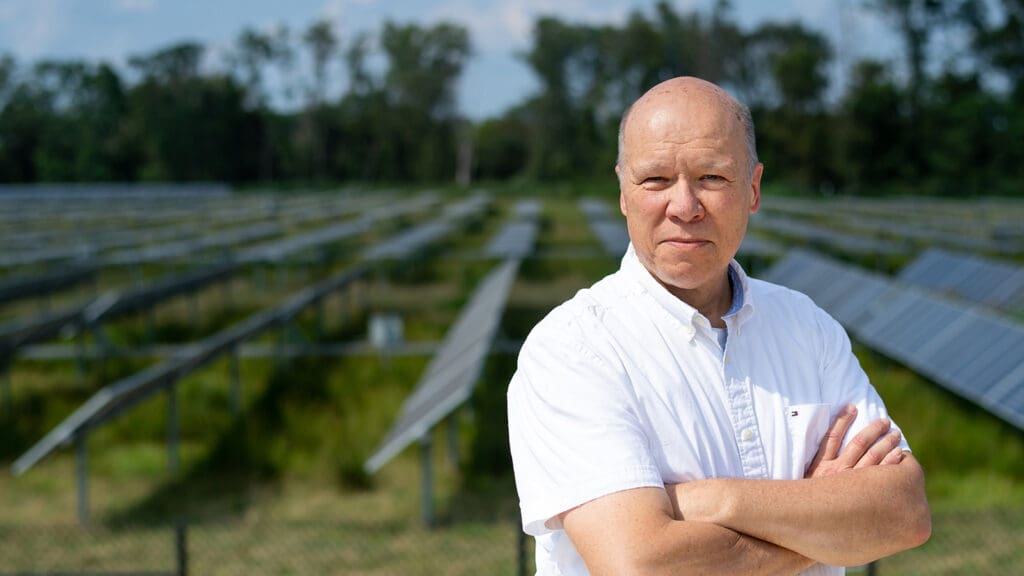 Man stands in front of large array of solar panels.