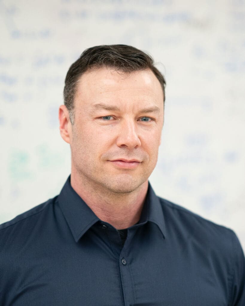 A man in a blue shirt standing in front of a whiteboard.