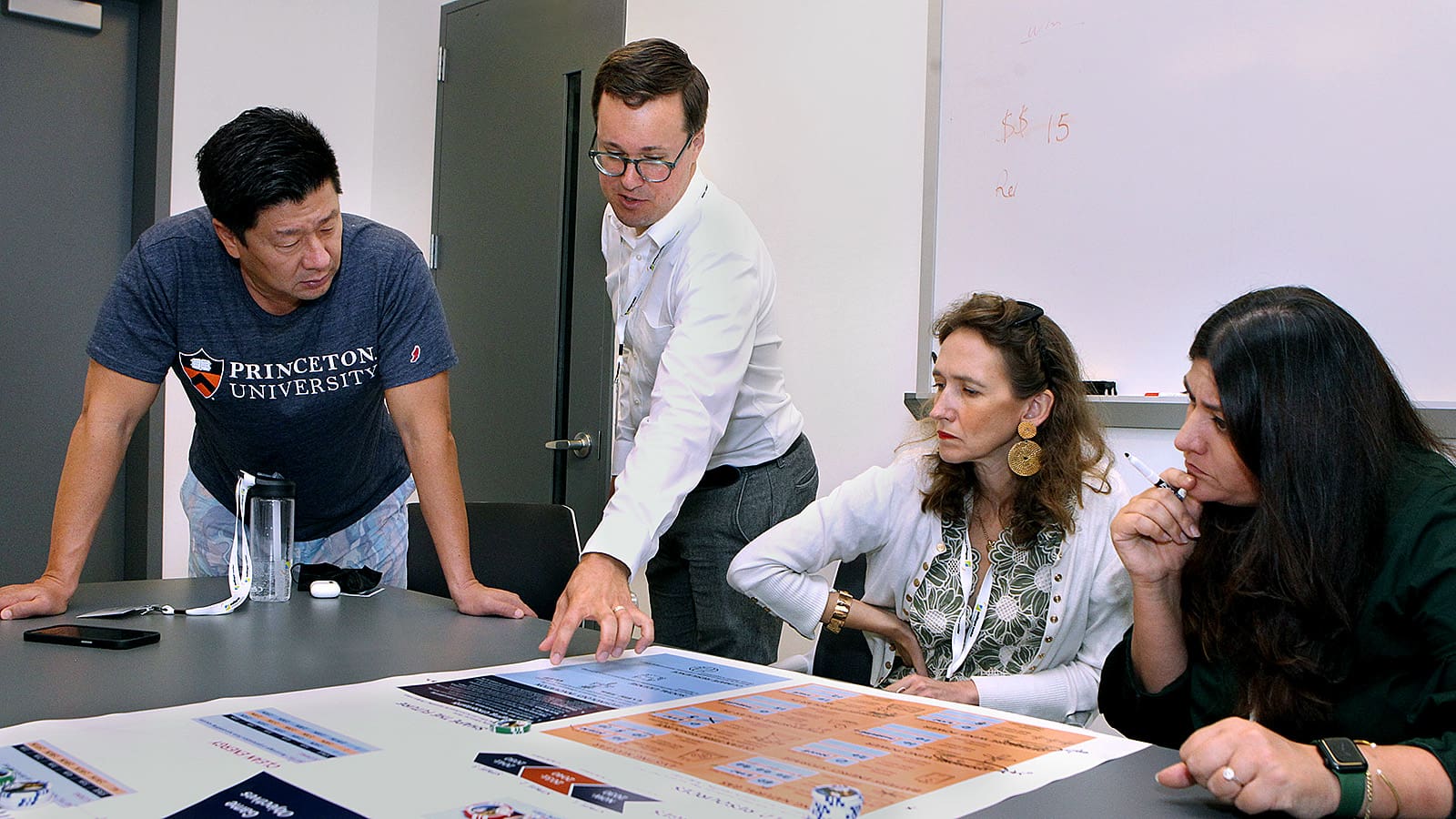 Man points at chart on a table while several two women and a man watch.