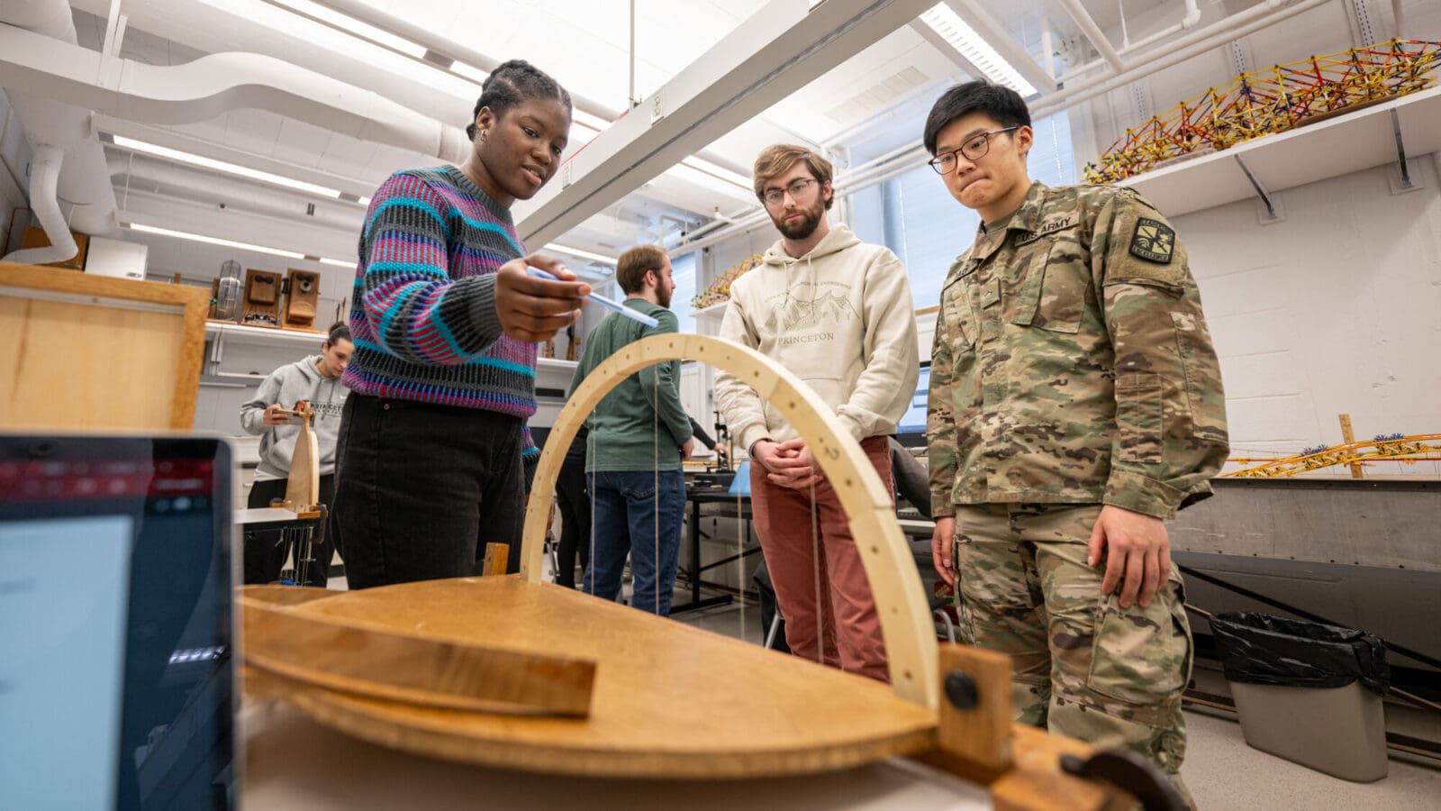 A group of three people examine a wooden model of a bridge.