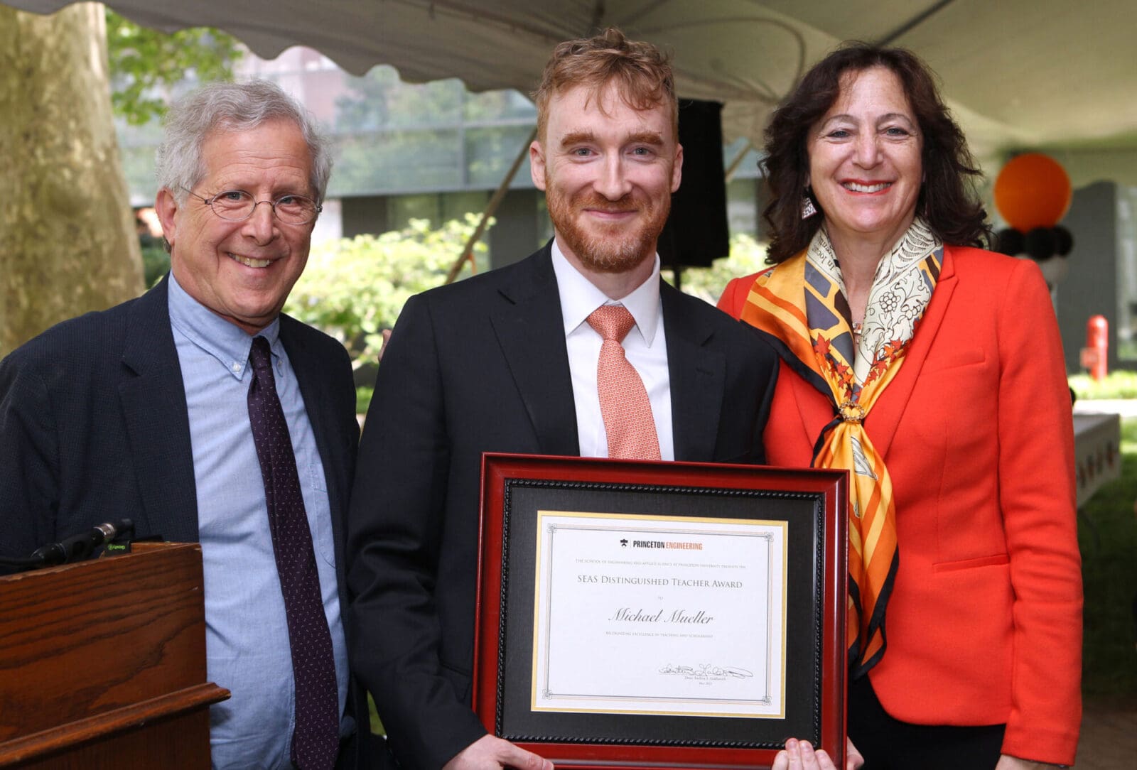 A man proudly holding an award with two colleagues at his side.