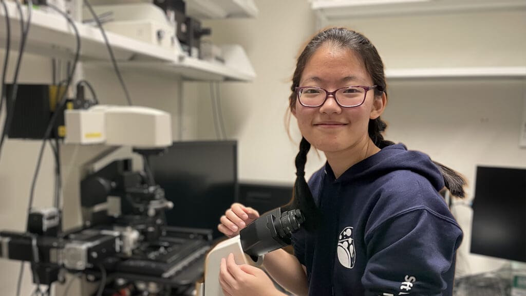 A smiling woman sitting at a lab bench with equipment
