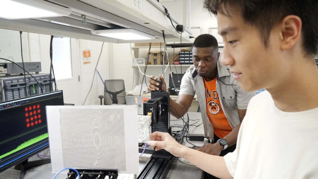 Two men at a lab bench working with a highly patterned paper sheet.