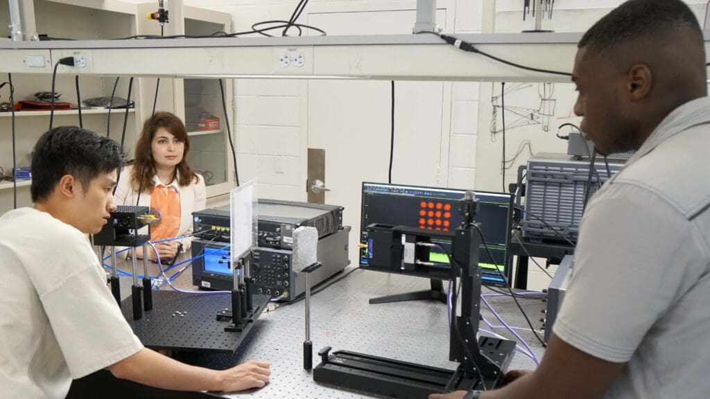 Two men and a women hold a discussion across a lab bench