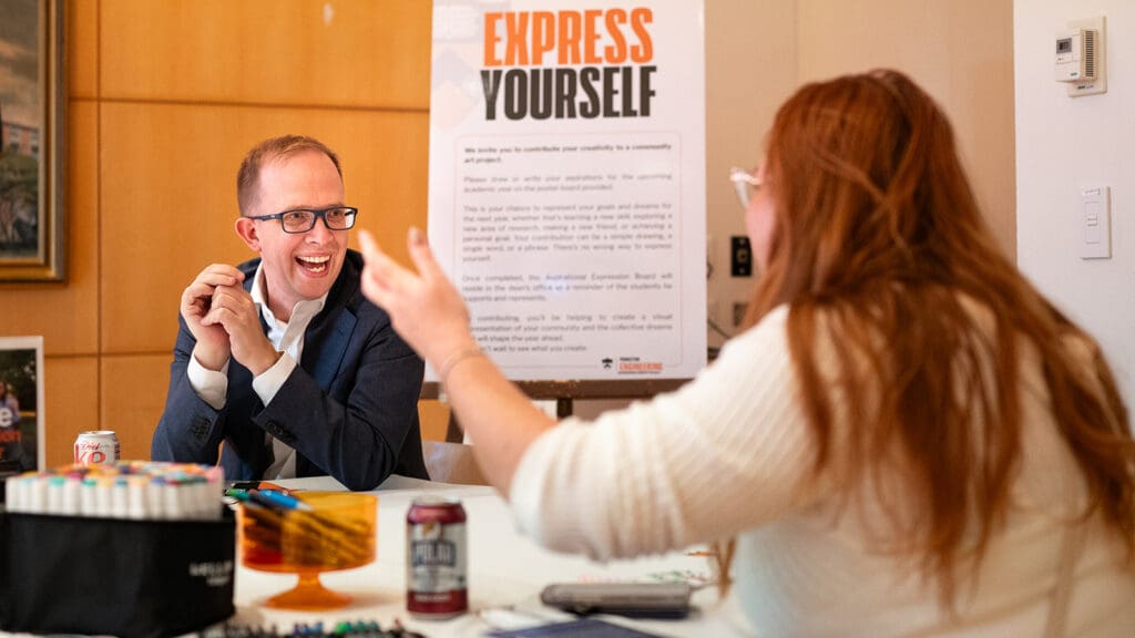 Woman in foreground, seen from back, speaks to man who is facing her and smiling.