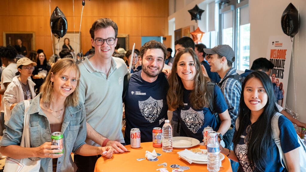 Group of five graduate students standing at a table.