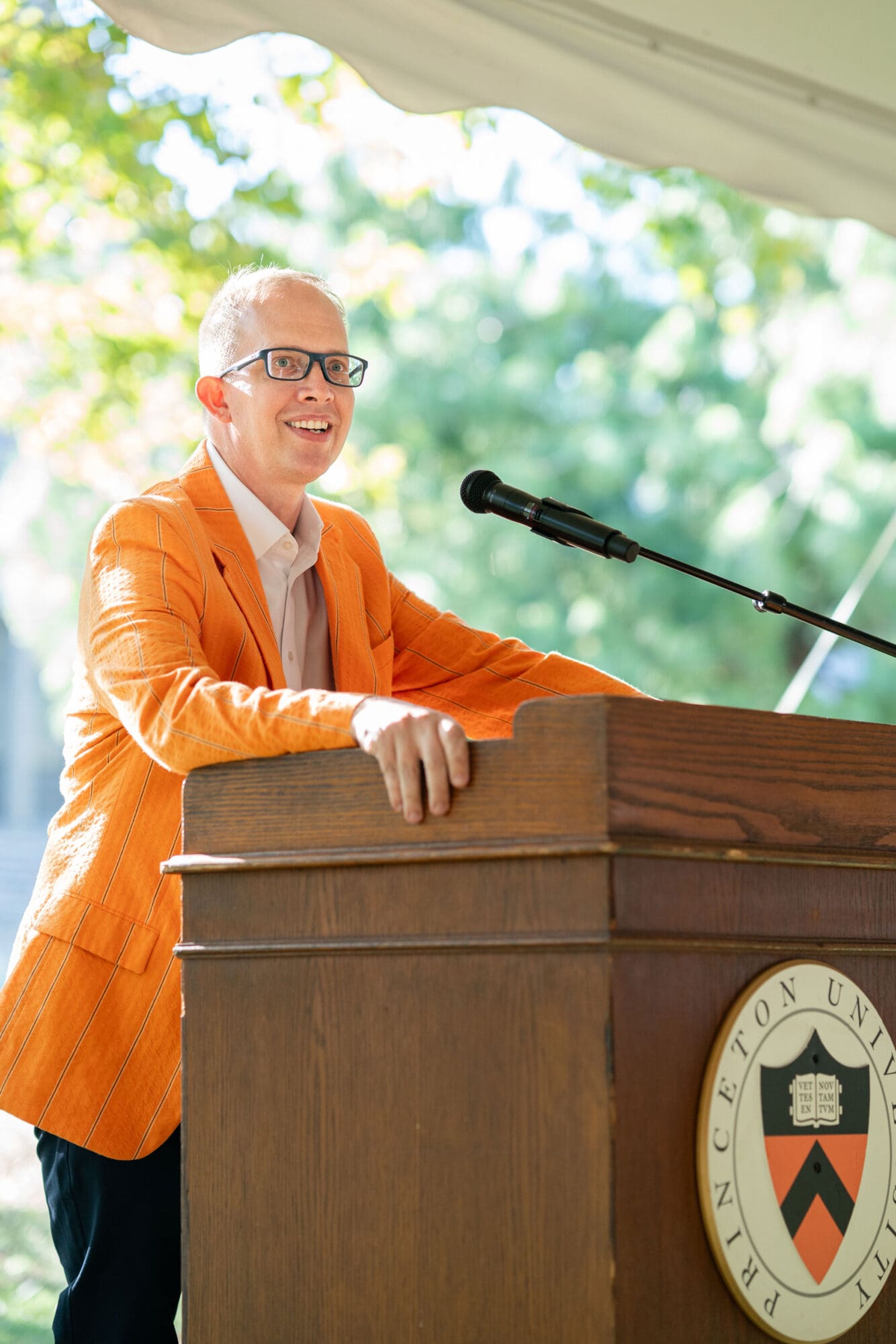 A man wearing an orange jacket speaks at a podium.