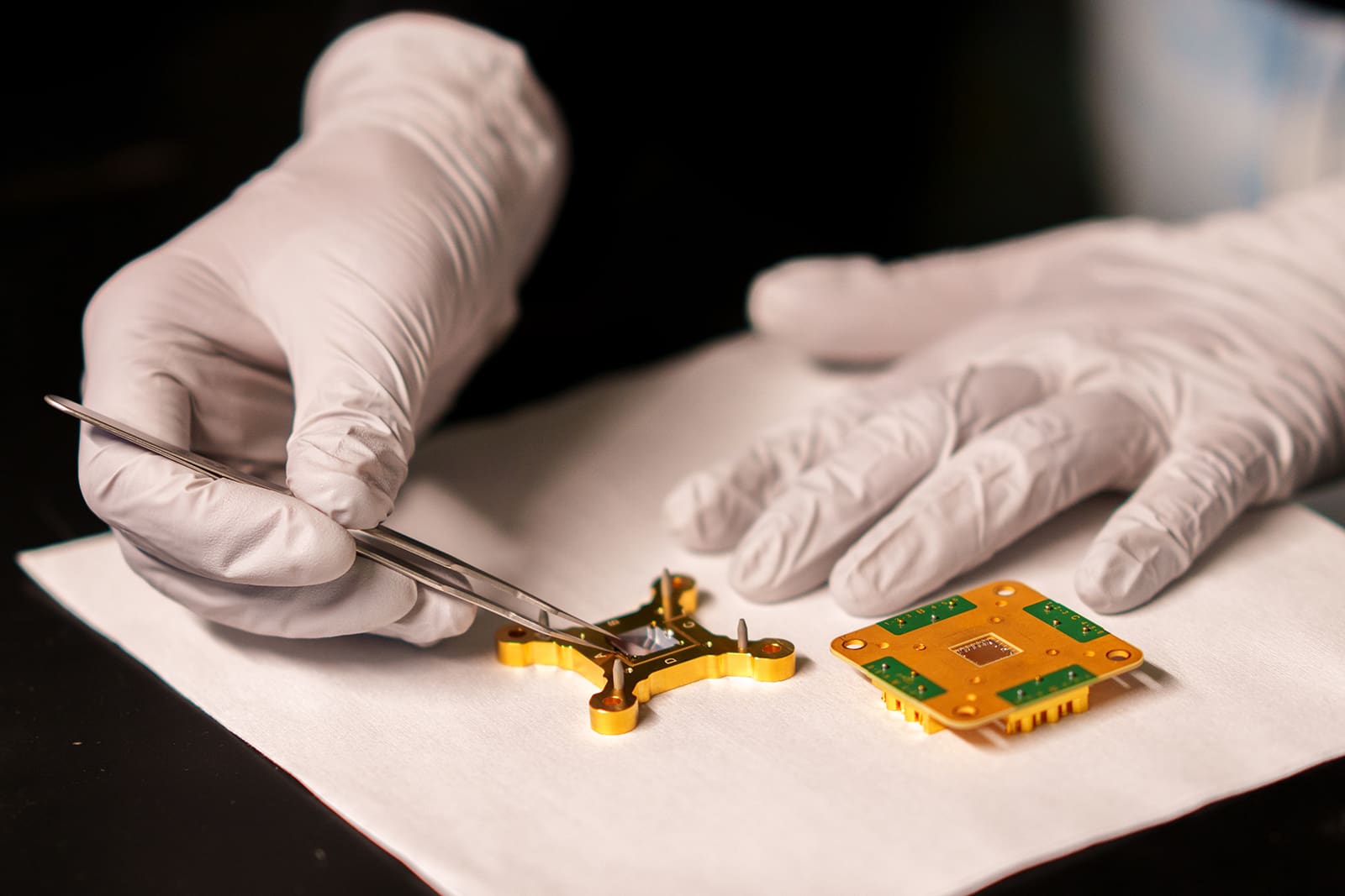 Gloved hands use tweezers to place a chip in its package.