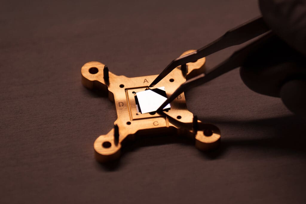 Tweezers place a quantum computing chip into its larger packaging.