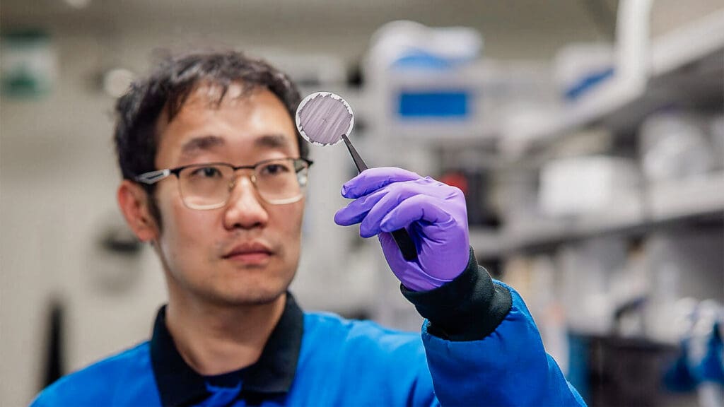 A researcher holds up a circular disc with tweezers